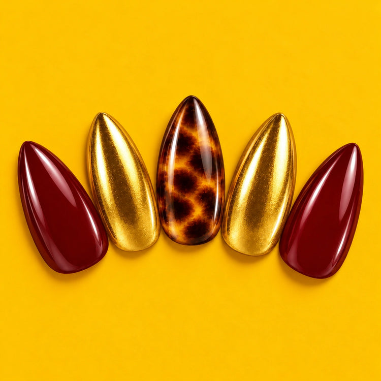 On Me press-on nails fanned out on mustard yellow: burgundy, tortoiseshell and gold almond nails.